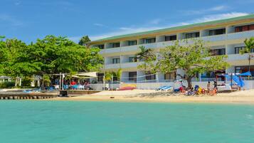 A beachfront hotel with multiple balconies, a sandy beach, and a pool area.