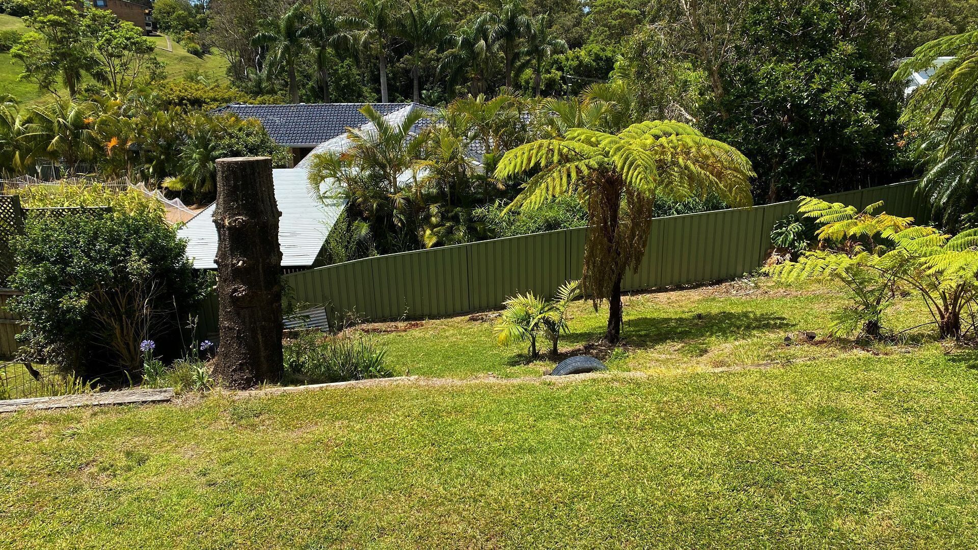 A residential property with a fenced yard, a large tree, and a house with a sloped roof.