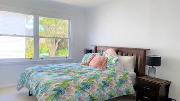 A bedroom with a bed, a nightstand, a window with blinds, and a view of trees outside.