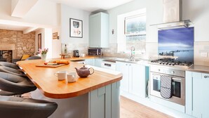 A modern kitchen with a central island, built-in appliances, and a stone accent wall. - Polly's Folly (Swanage)