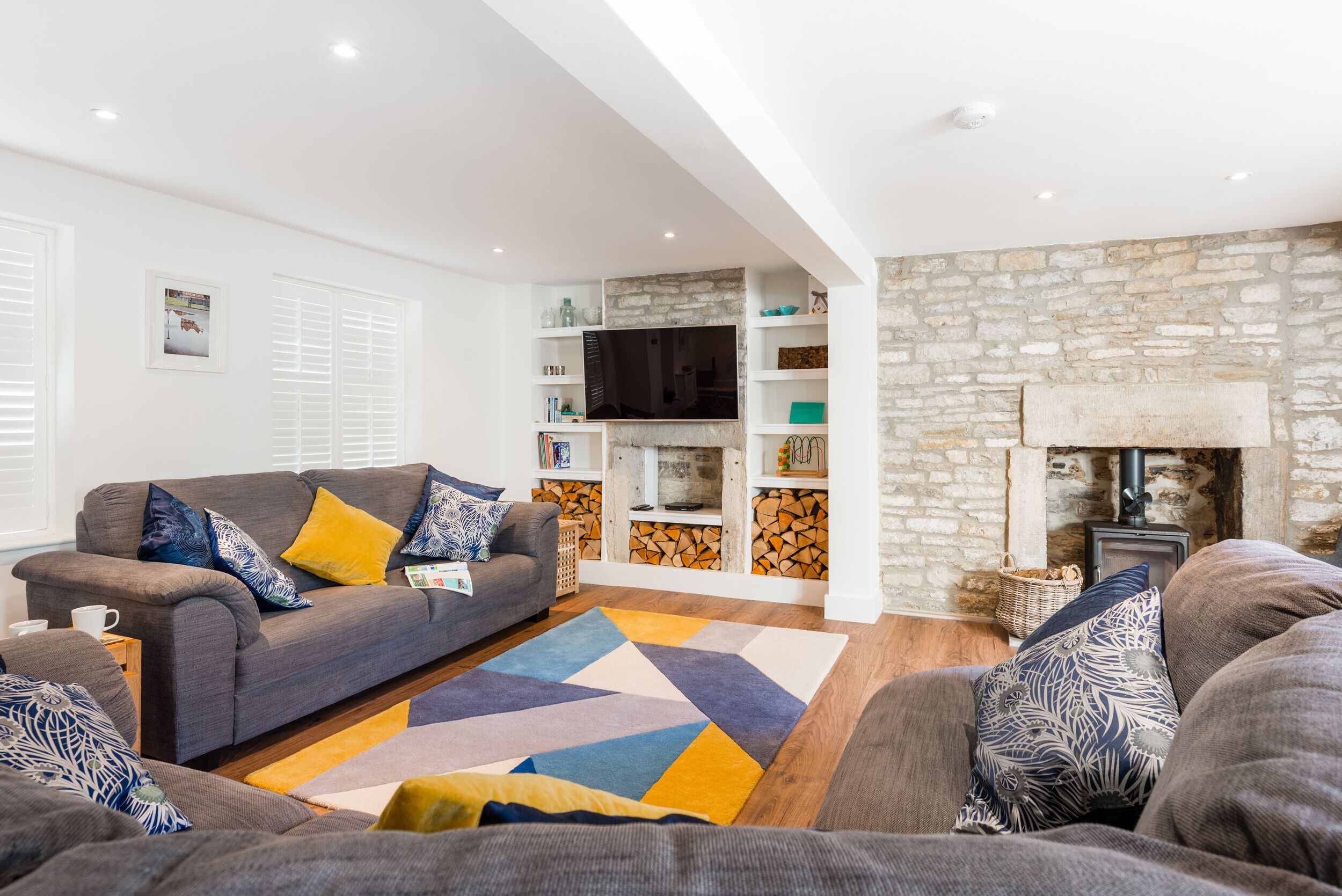 Ein modernes Wohnzimmer mit grauem Sofa, einem gemusterten Teppich und einer Steinwand mit Kamin.