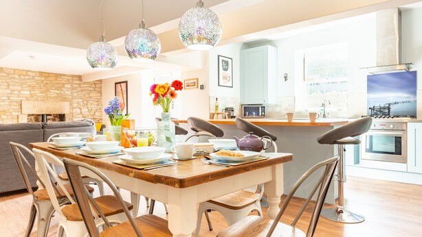 A modern kitchen with a dining area, featuring a wooden table, chairs, and pendant lights. - Polly's Folly (Swanage)