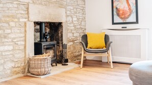 A cozy living room with a stone fireplace, a modern chair with a yellow cushion, and a framed artwork on the wall. - Polly's Folly (Swanage)