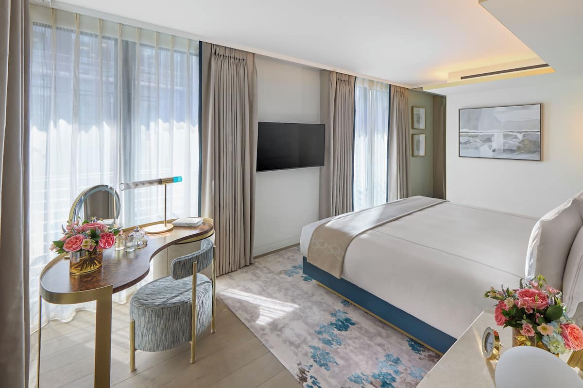 Habitación de hotel con cama, escritorio con espejo, silla, televisor y ventana con cortinas.