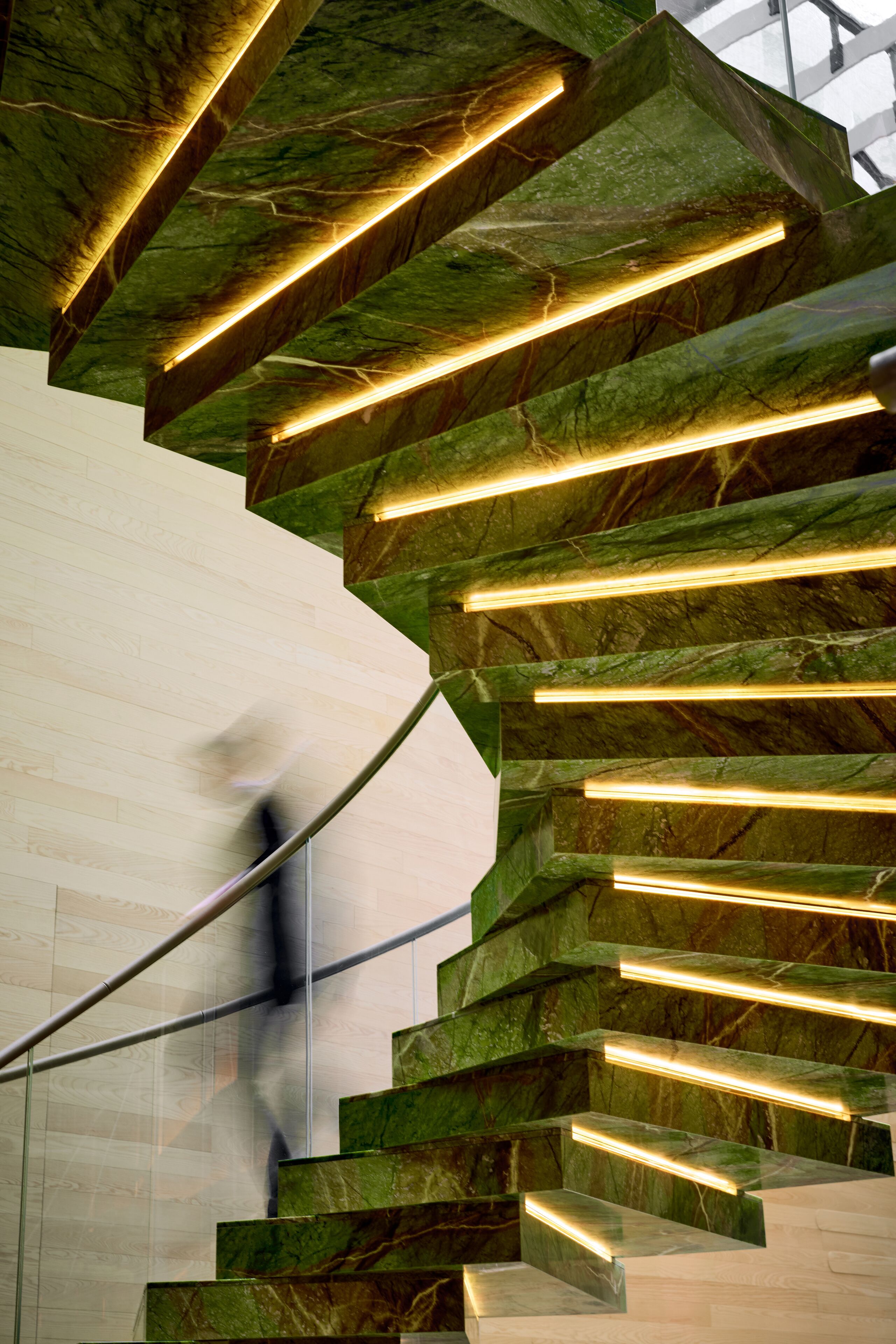 A spiral staircase with green marble steps and illuminated handrails.