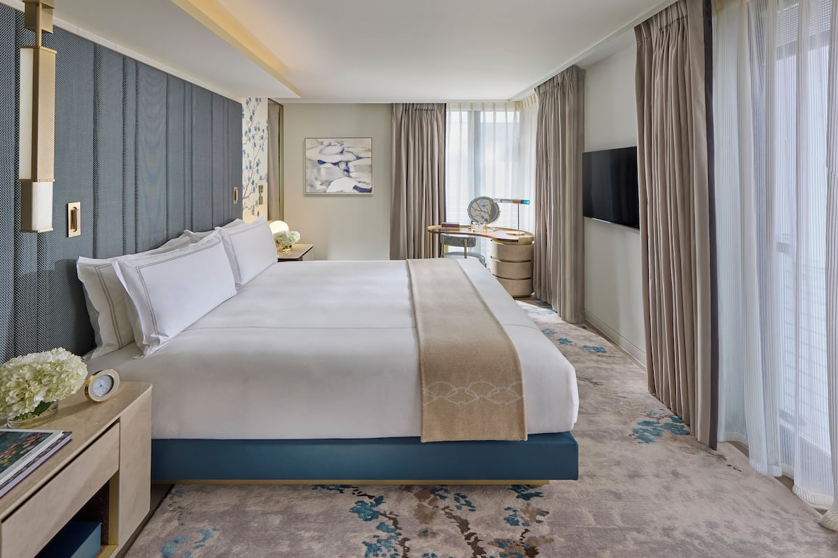 Una habitación de hotel moderna con una cama grande, un escritorio, un televisor y una ventana con cortinas.
