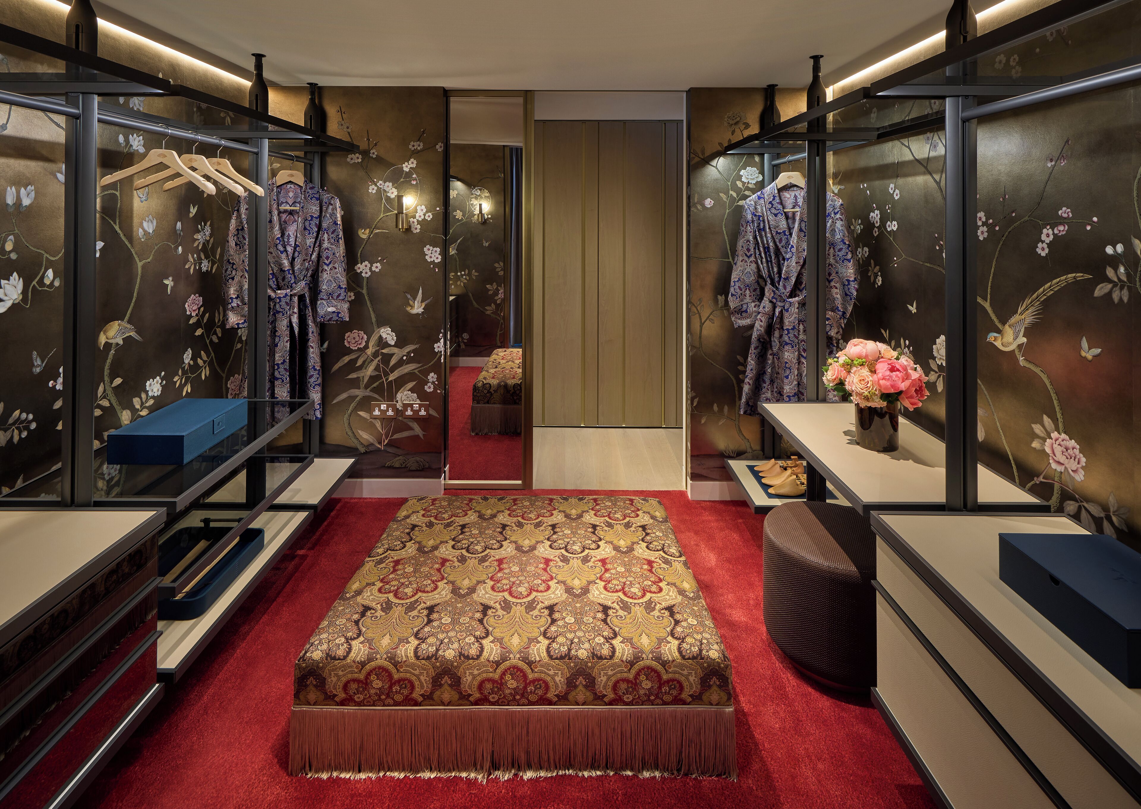 A bedroom with a red carpet, a patterned bedspread, and a mirror with floral wallpaper.