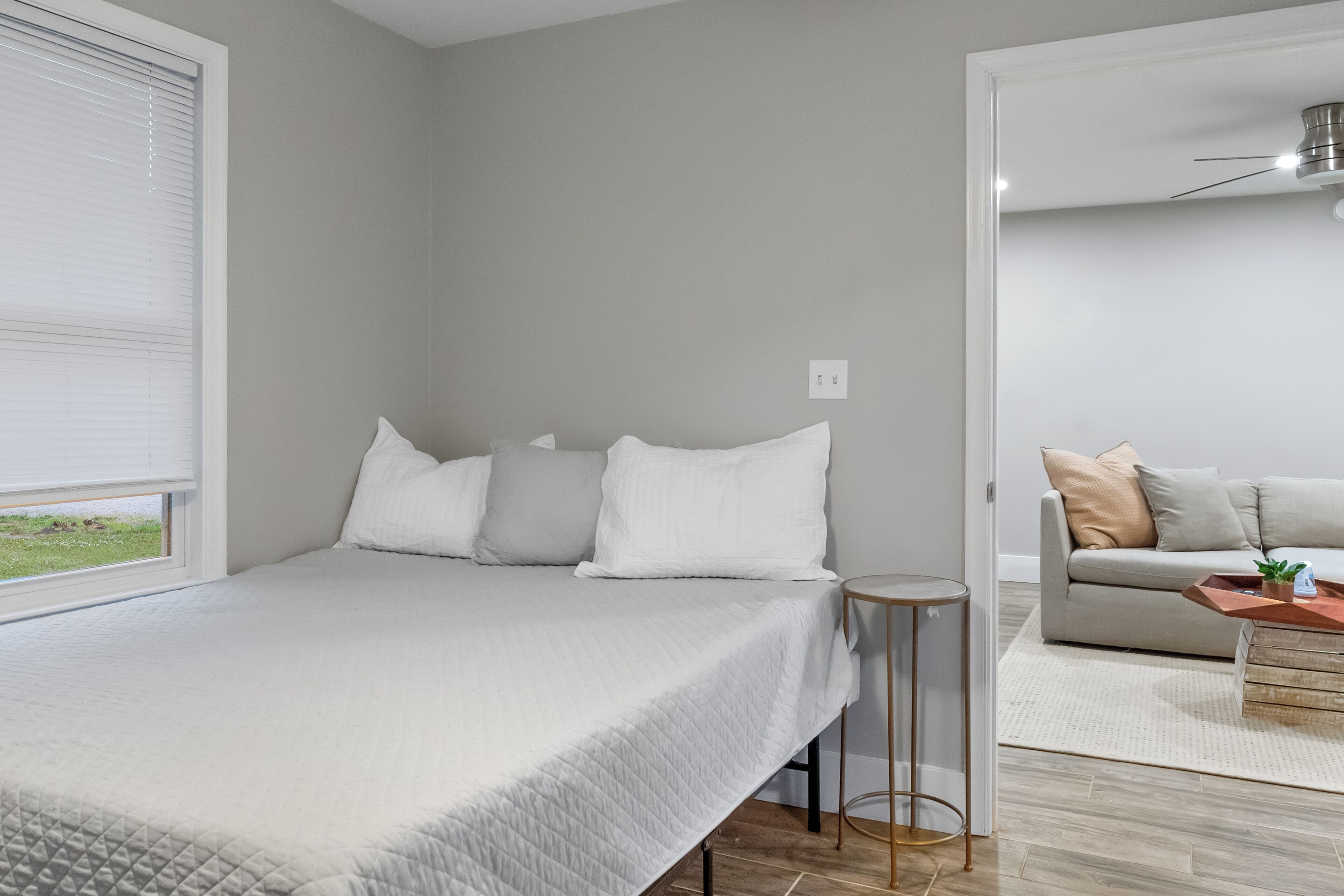 A bedroom with a bed, a bedside table, and a view of a living area with a sofa and a coffee table.