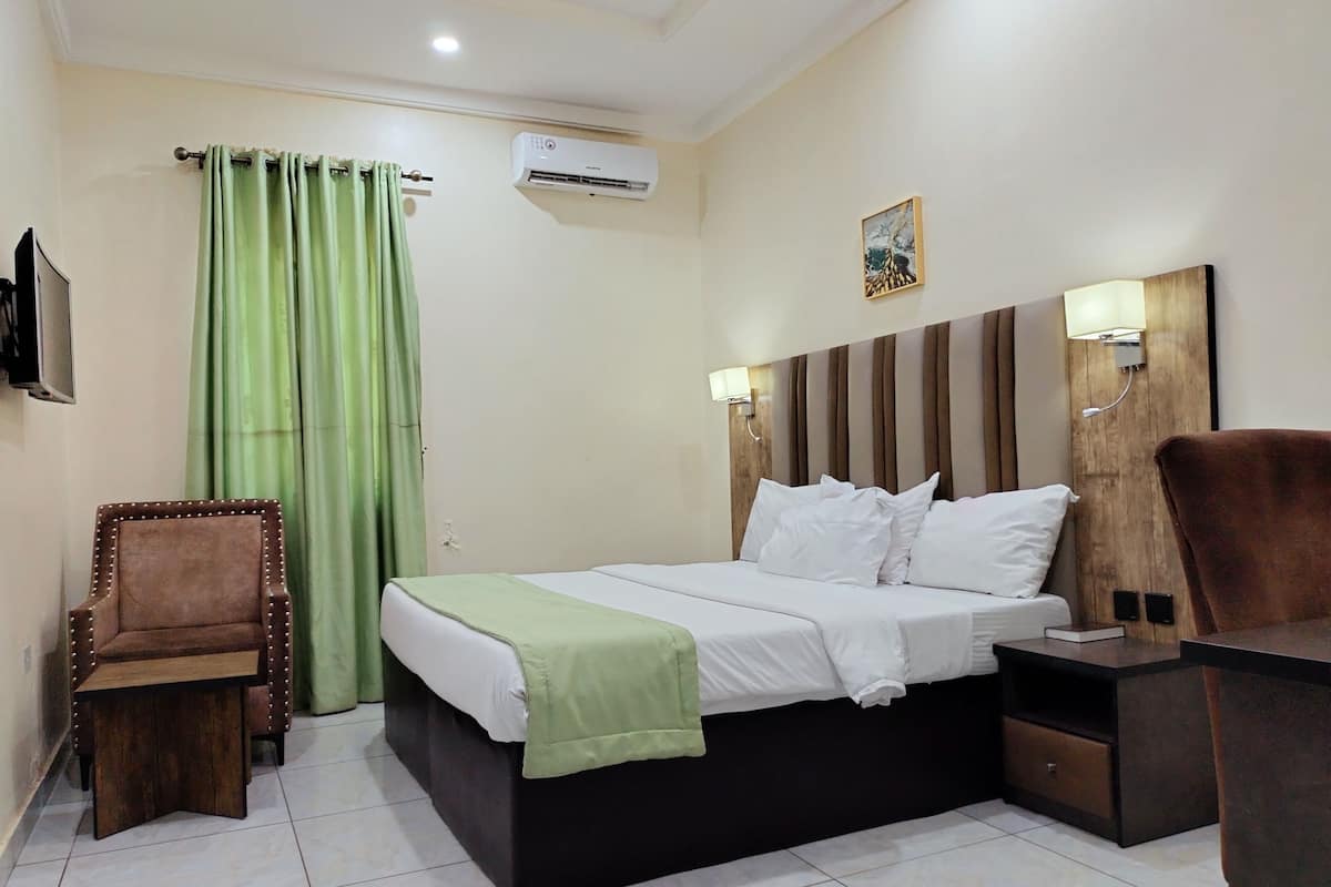 A hotel room with a bed, a chair, a desk, a TV, and an air conditioner.