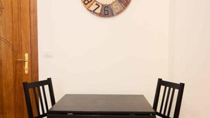A dining area with a wooden table and four chairs, a wall clock, and a wooden door. - Sunrise Studio Apartment (Napoli)