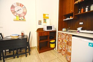 Een kleine keuken met een magnetron, een koelkast en een klok aan de muur.
