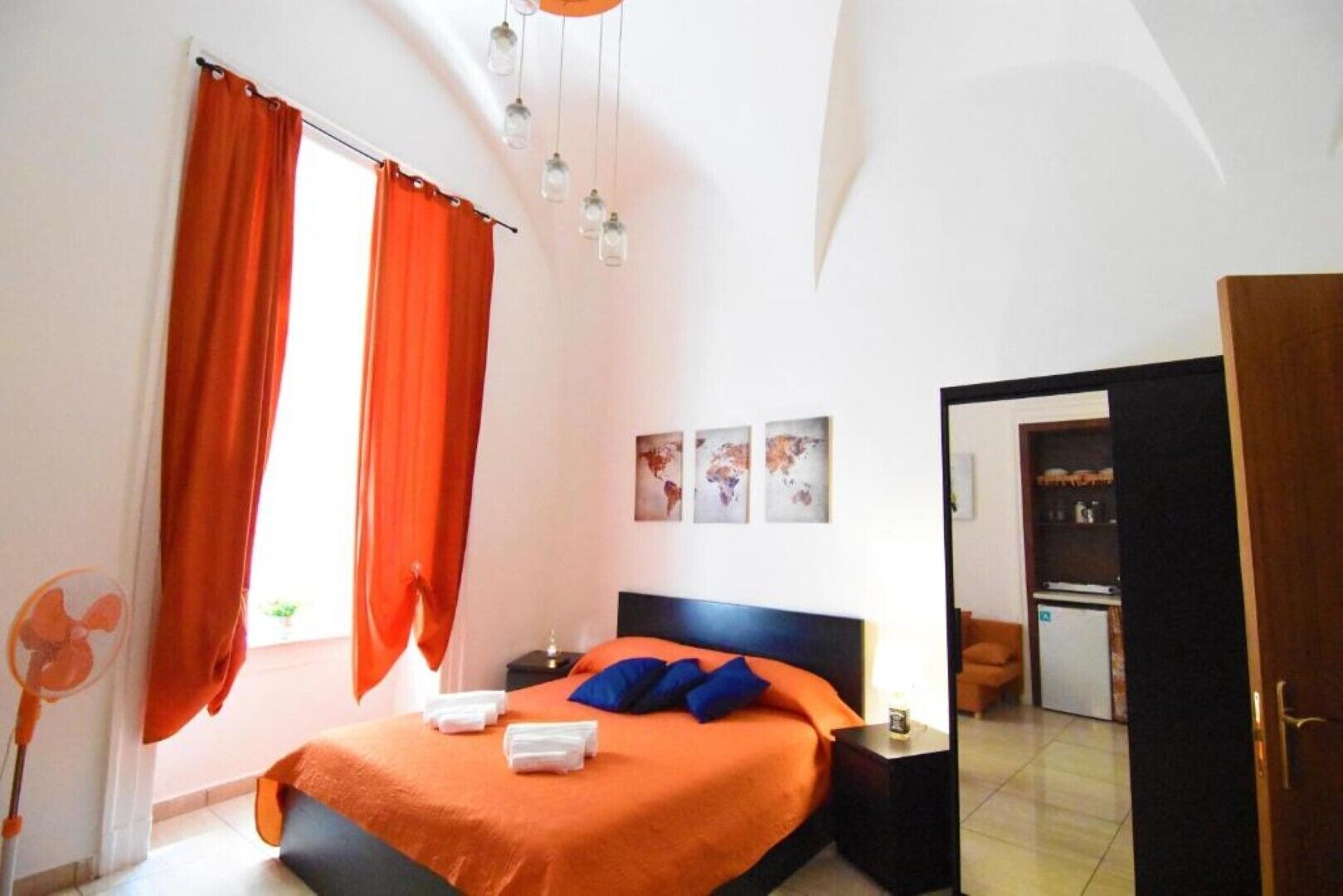 A bedroom with a bed, orange curtains, a nightstand, and a door leading to another room.