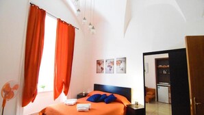 A bedroom with a bed, orange curtains, a nightstand, and a door leading to another room. - Sunrise Studio Apartment (Napoli)