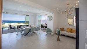 A modern living room with a sofa, dining area, and a view of the ocean. - Villa Roxy, Fantastic 3BDR Seafront Protaras Villa with Pool (Protaras)