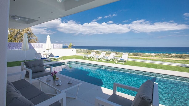 A modern outdoor pool area with lounge chairs, a table, and a ceiling fan. - Villa Roxy, Fantastic 3BDR Seafront Protaras Villa with Pool (Protaras)