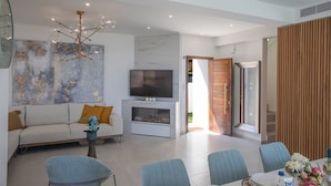 A modern living room with a sofa, TV, and dining area. - Villa Roxy, Fantastic 3BDR Seafront Protaras Villa with Pool (Protaras)