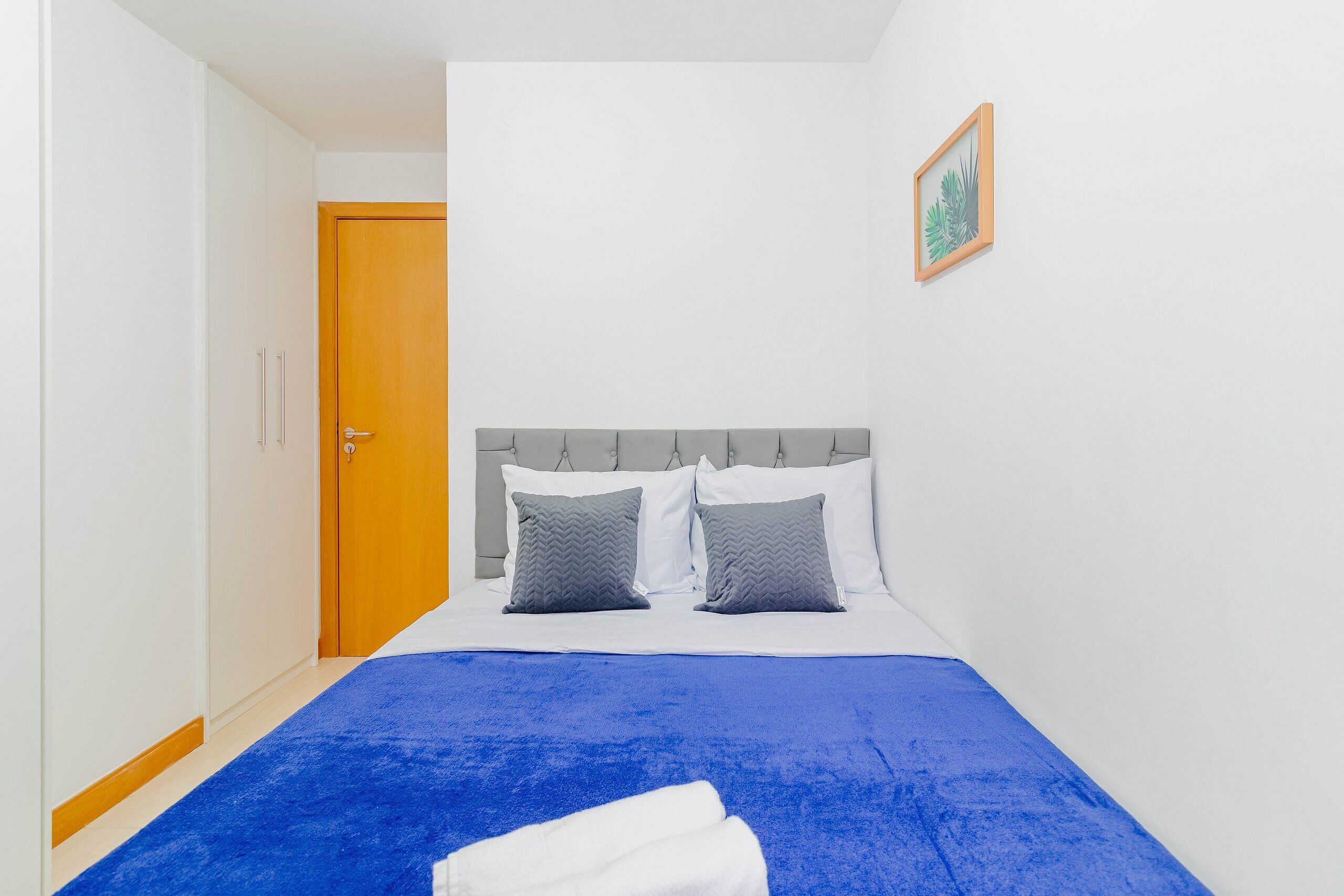 A bedroom with a bed, a door, and a framed picture on the wall.