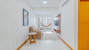 A modern hallway with a sofa, a small round table, and a view of the outside through a glass door. - BR07 Apto a 550m da Praia da Barra (Salvador)