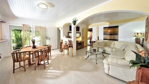 Uma sala de estar ampla com uma mesa de jantar redonda de madeira, sofás bege e uma mesa de centro.