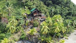 Ein Holzhäuschen mit Balkon, umgeben von üppiger Vegetation und Palmen.
