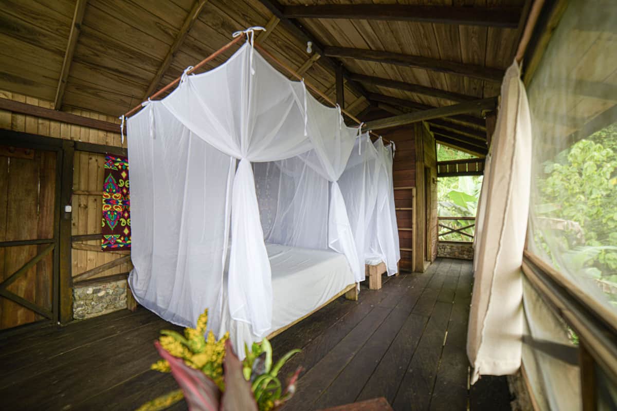 A wooden room with a bed covered by white mosquito nets.