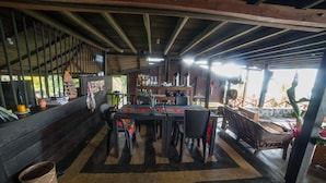 Ein rustikales Holzinterieur mit einem Essbereich, der einen Tisch und Stühle umfasst, einer Bar mit Regalen voller Flaschen und Blick ins Grüne.