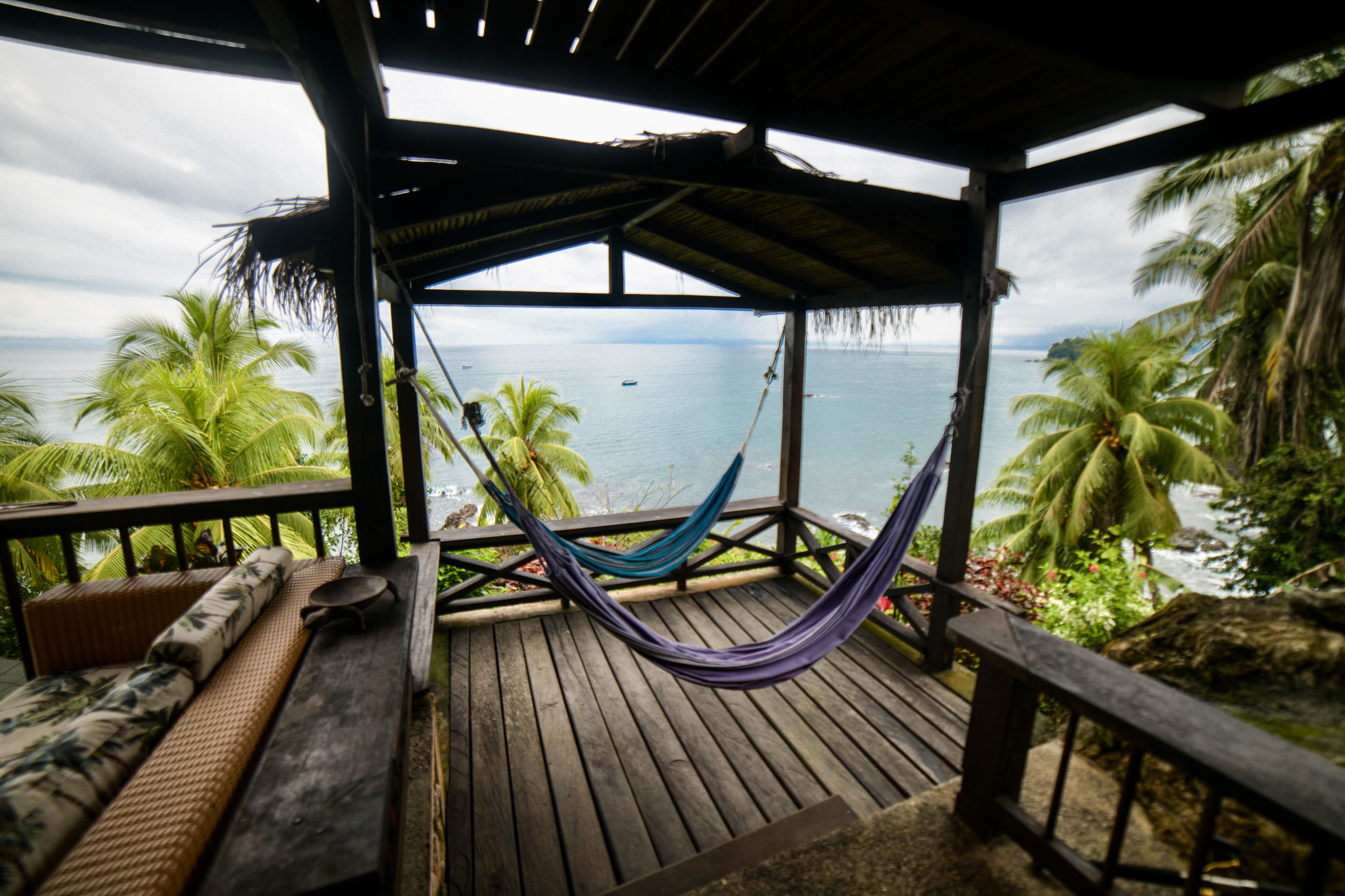 A wooden deck with a hammock, a bench, and a view of the ocean.