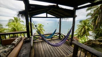 A wooden deck with a hammock, a bench, and a view of the ocean.
