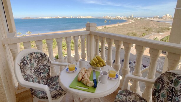 A balcony with a table set for breakfast, overlooking a coastal cityscape. - Playa Paraíso apartment with lovely Mar Menor views (Playa Paraiso)