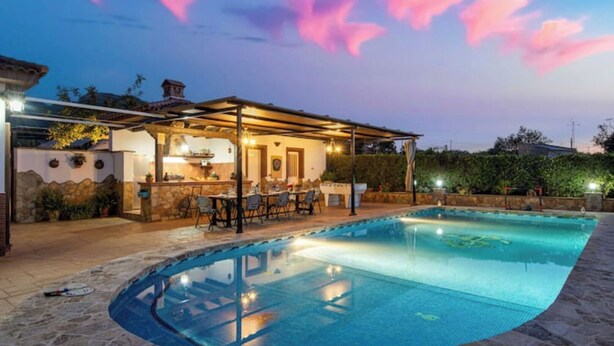 Une piscine dotée d’un patio couvert, d’un revêtement de sol en pierre et d’un bar avec des places assises à l’extérieur.