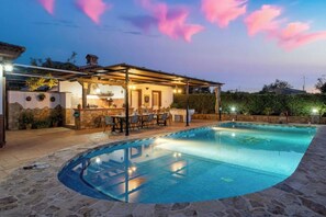 A swimming pool with a covered patio area, stone flooring, and a bar with outdoor seating.