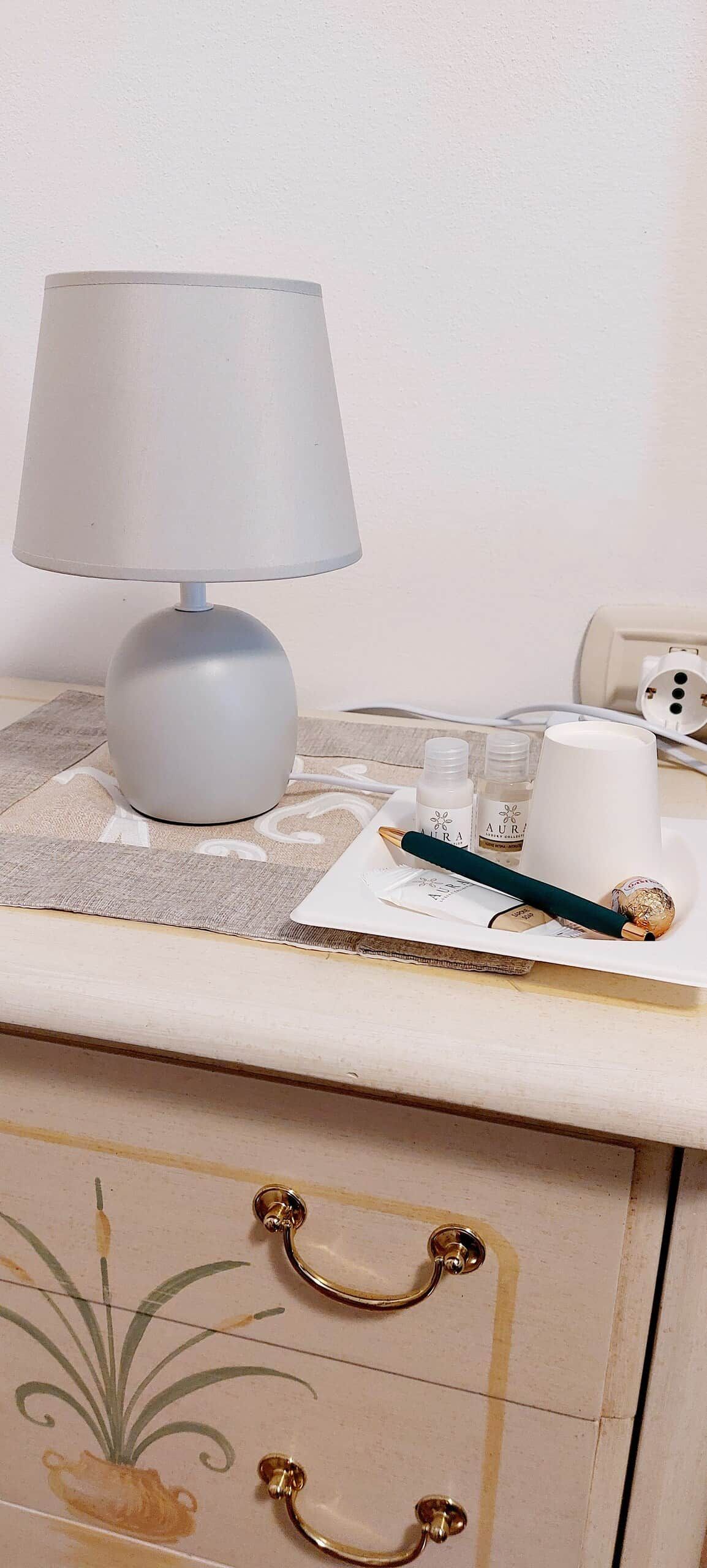 A bedside table with a lamp, a tissue box, a pen, and a small bottle.