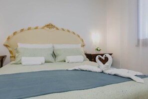 Un letto rifatto con cuscini e una coperta blu, una decorazione a forma di cuore con un asciugamano e un punto luce fissato al muro.