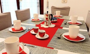 Zona pranzo con tavolo rotondo apparecchiato per un pasto, corredata da caffettiera, tazze e posate.