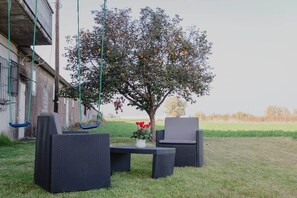 An outdoor seating area with wicker furniture, a table with a potted plant, and a tree with fruit. - To complete (Veneto)