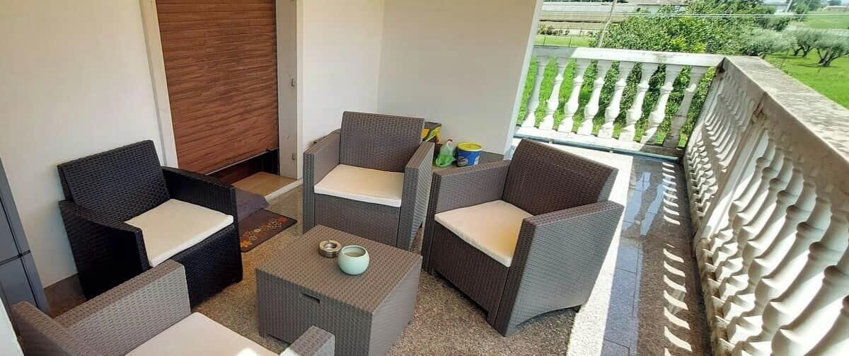 A balcony with wicker furniture, a small table, and a view of greenery.