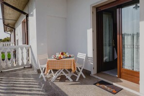 Un balcone con un tavolo apparecchiato per due, una sedia bianca e una porta in legno con un pannello di vetro.