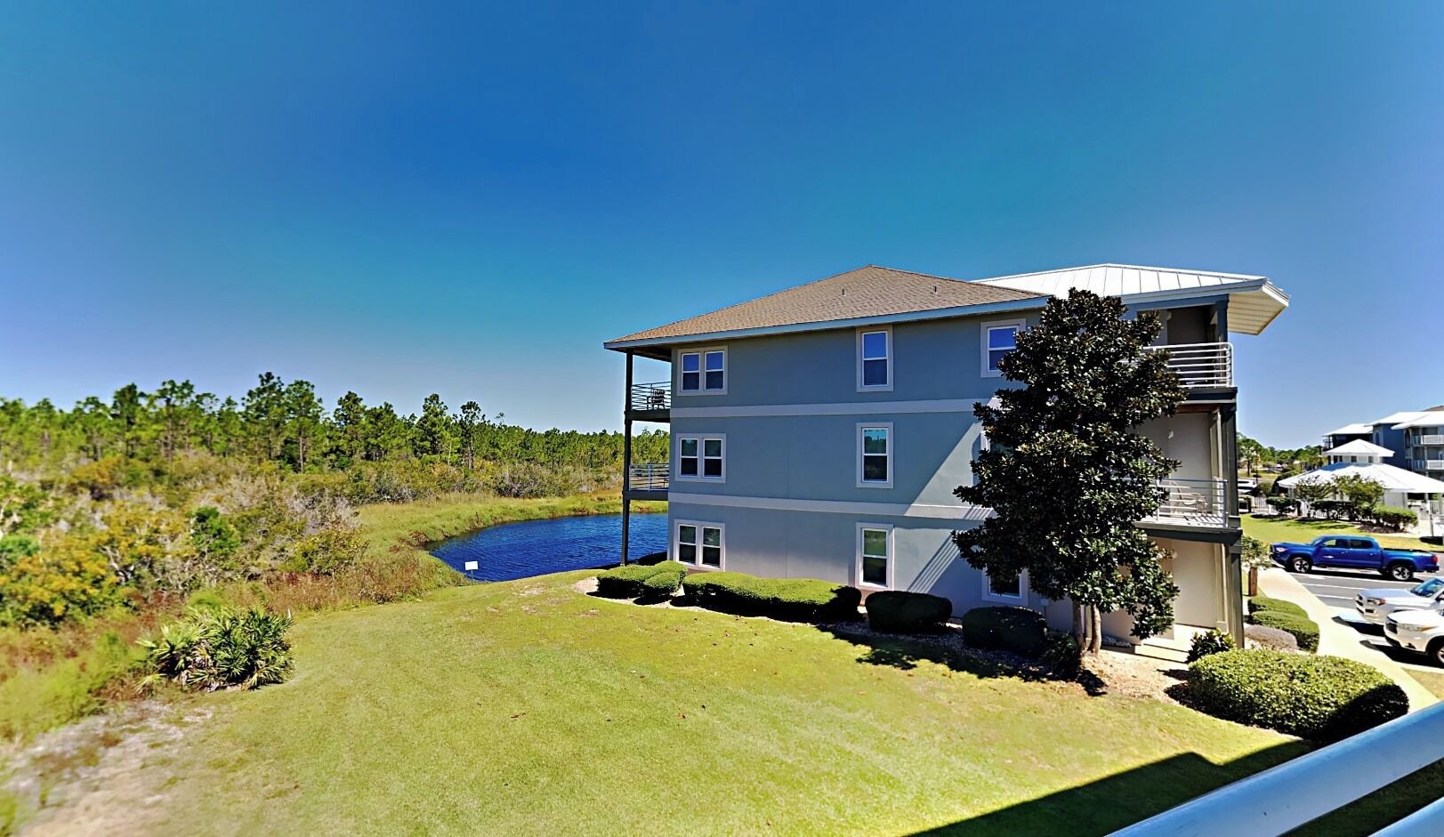 A multi-story building with a flat roof, a balcony on the upper floor, and a small pond in the foreground.
