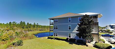A multi-story building with a flat roof, a balcony on the upper floor, and a small pond in the foreground.