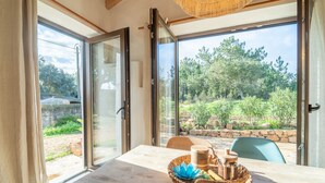 A room with a wooden table, a woven basket with items, and a view of a garden through large glass doors.
