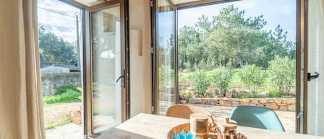 A room with a wooden table, a woven basket with items, and a view of a garden through large glass doors.