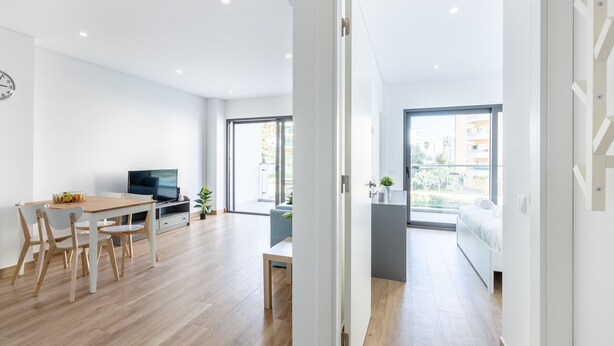 Eine moderne Wohnung mit Essbereich, Fernseher und einem Balkon mit Blick auf Gebäude.