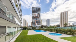 Ein moderner Apartmentkomplex mit gepflegtem Rasen, zwei Schwimmbecken und Hochhäusern im Hintergrund.