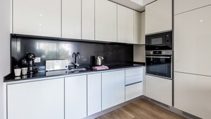 Eine moderne Küche mit weißen Schränken, einer schwarzen Arbeitsplatte, einer Kaffeemaschine, einem Wasserkocher und einer Mikrowelle.