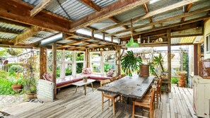 Ein rustikaler Essbereich aus Holz mit einer Bank und einem Tisch, umgeben von Topfpflanzen und Blick auf den Garten.