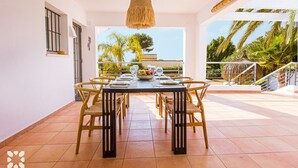 Een eetgedeelte met een tafel gedekt voor vier personen, omringd door rieten stoelen, met uitzicht op palmbomen en een gebouw op de achtergrond.