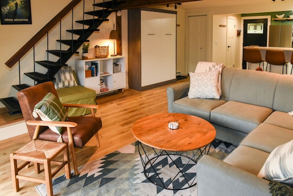 A modern living room with a staircase, a sofa, a coffee table, and a bookshelf.