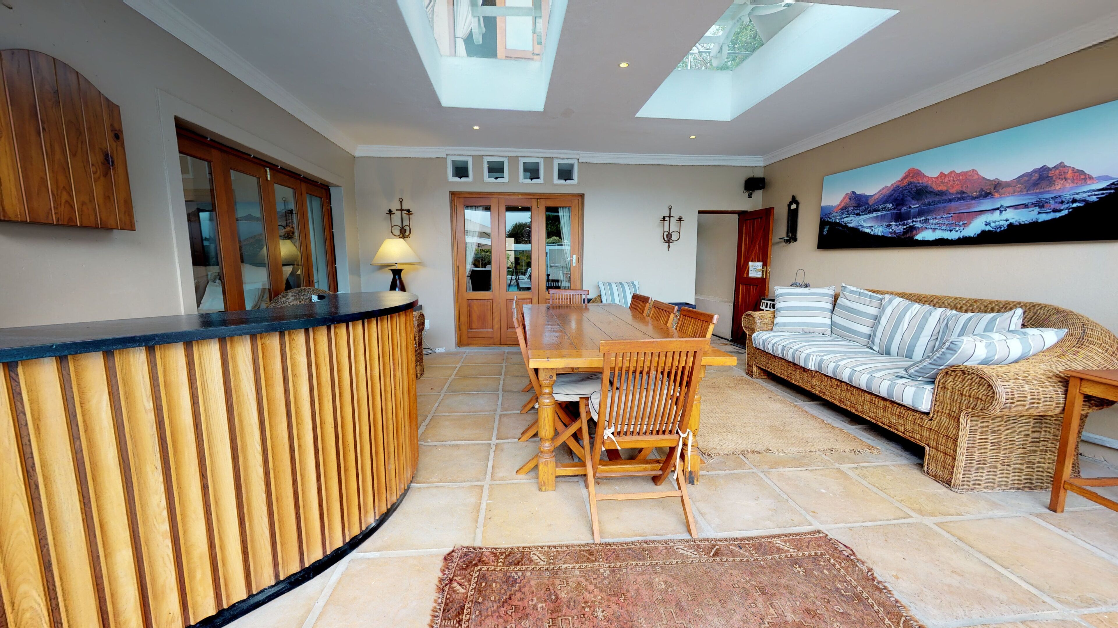 A spacious living area with a wooden reception desk, a dining table with chairs, a sofa, and a large window with a mountain view.