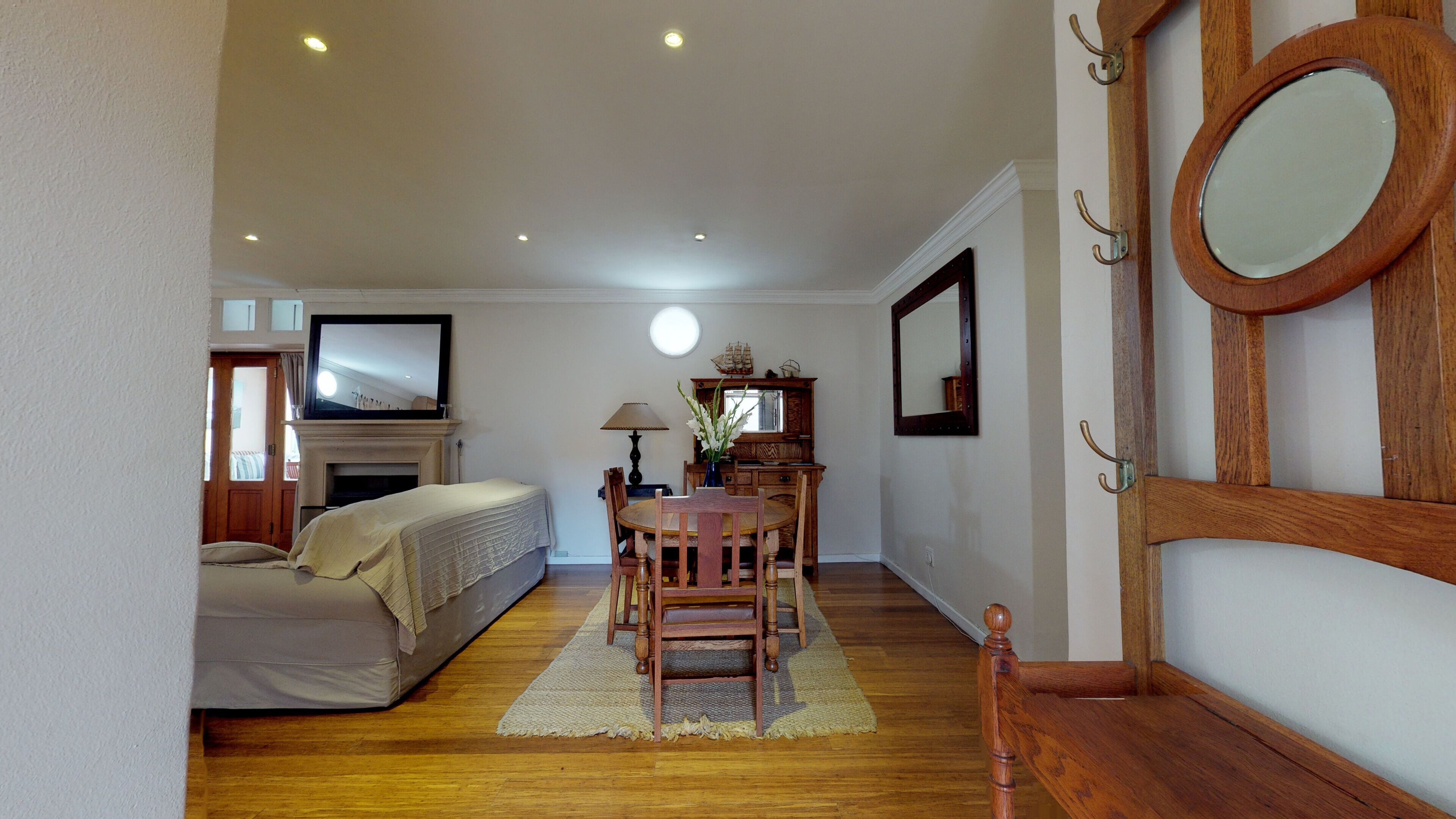 Une chambre à coucher avec un lit, un bureau et une chaise. Il y a un miroir au mur et une fenêtre avec des rideaux.