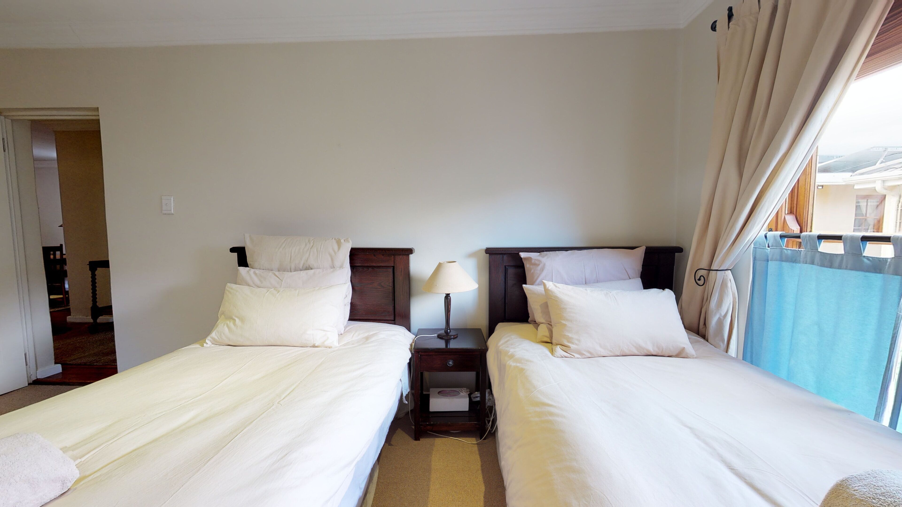 Et hotelværelse med to senge, et natbord med lampe og udsigt udad.